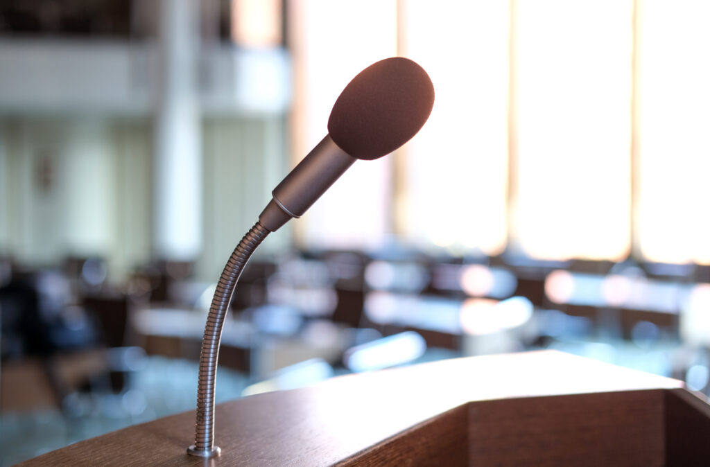 Konzept Kommunikation: Leerer Konferenzsaal oder Sitzungsraum mit Fokus auf das Mikrofon des Rednerpultes im Gegenlicht